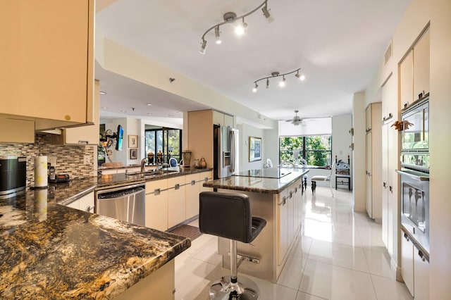 kitchen with stainless steel appliances, a sink, backsplash, ceiling fan, and a kitchen island