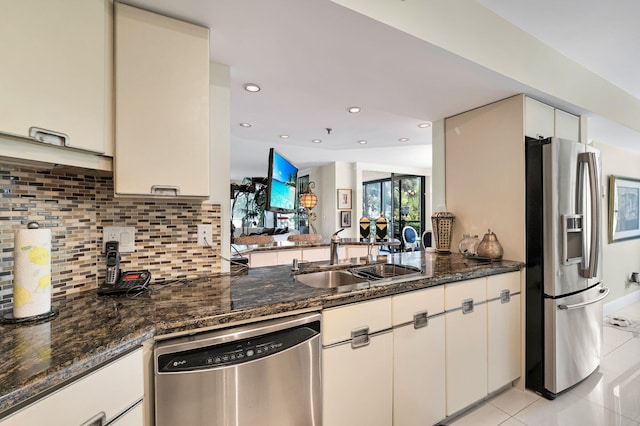 kitchen featuring appliances with stainless steel finishes, a sink, light tile patterned floors, backsplash, and dark stone counters