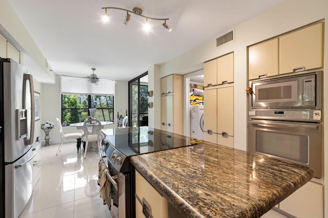 kitchen featuring appliances with stainless steel finishes, cream cabinetry, ceiling fan, washer / dryer, and light tile patterned floors