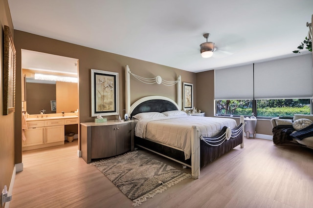 bedroom featuring light wood finished floors, ensuite bathroom, baseboards, and a ceiling fan