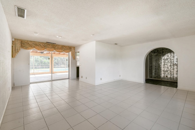 unfurnished room with a textured ceiling, arched walkways, baseboards, and light tile patterned floors