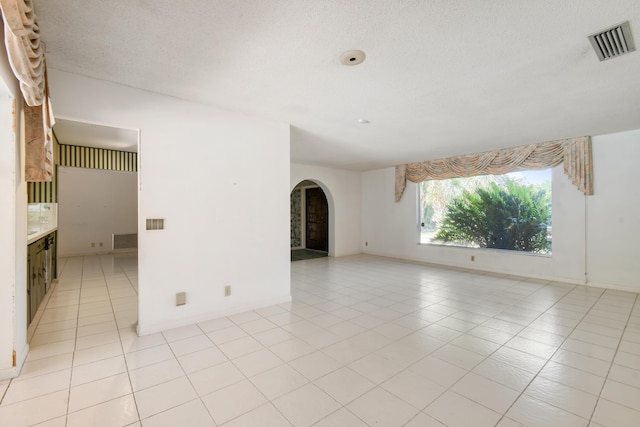 empty room with arched walkways, light tile patterned floors, a textured ceiling, and baseboards