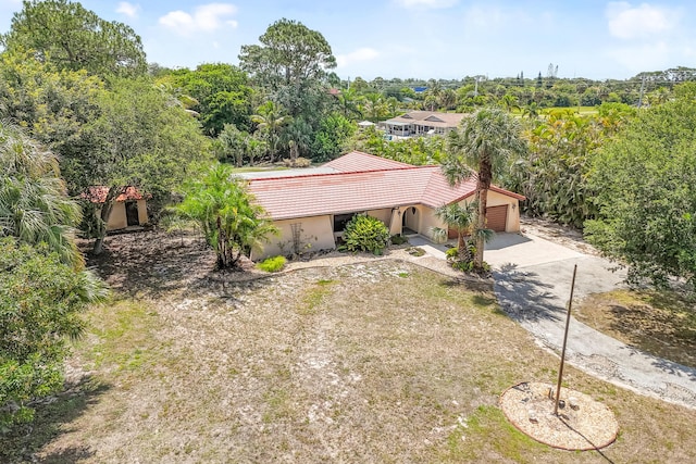 view of front of house featuring a tile roof, concrete driveway, an attached garage, stucco siding, and view of scattered trees