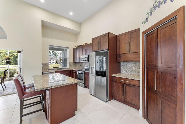 7793 Highlands Cir, Margate, FL 33063 - kitchen featuring appliances with stainless steel finishes, a towering ceiling, backsplash, light stone countertops, and a center island