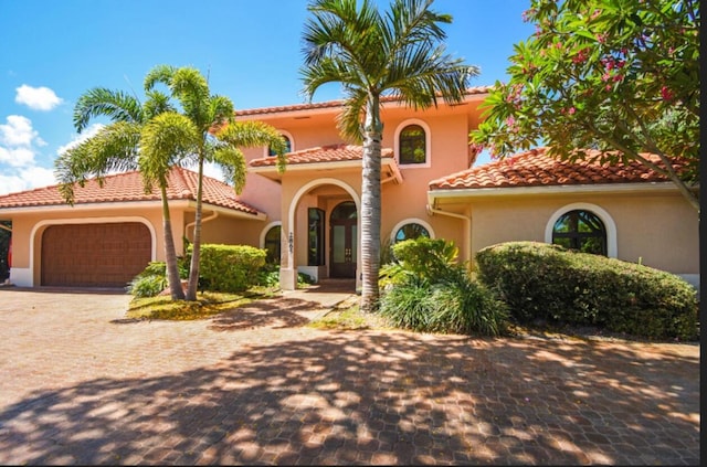 mediterranean / spanish house featuring stucco siding, a tile roof, a garage, and driveway