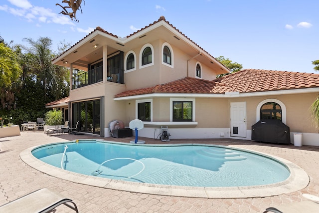 back of property featuring a balcony, a tile roof, an outdoor pool, a patio area, and stucco siding