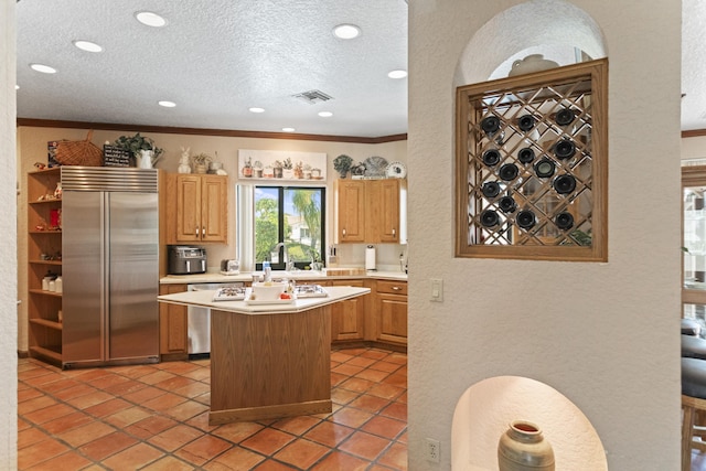 kitchen with appliances with stainless steel finishes, light countertops, a kitchen island, a textured wall, and a textured ceiling