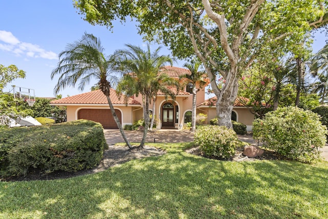 mediterranean / spanish home with stucco siding, a garage, a front yard, a tiled roof, and driveway