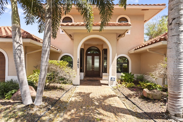view of exterior entry with french doors, a tiled roof, and stucco siding