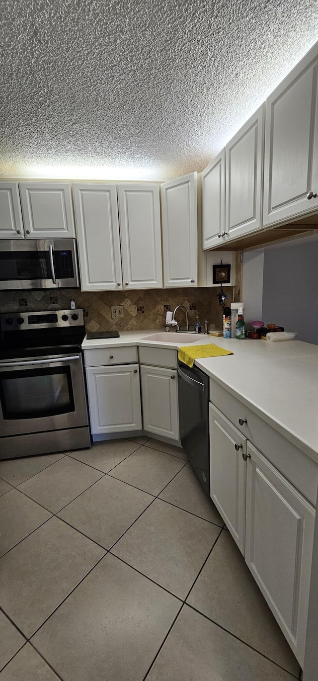 kitchen with appliances with stainless steel finishes, a textured ceiling, light tile patterned floors, white cabinetry, and light countertops