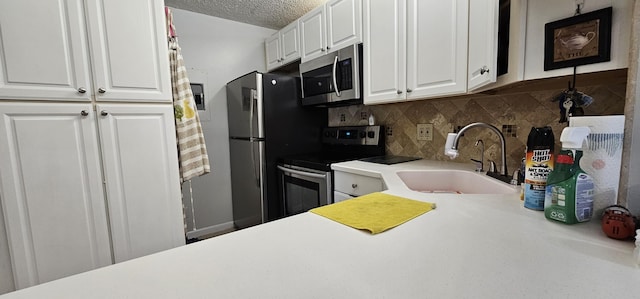 kitchen featuring appliances with stainless steel finishes, a sink, white cabinetry, tasteful backsplash, and light countertops