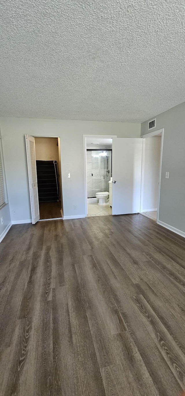unfurnished bedroom with wood finished floors, a textured ceiling, baseboards, and ensuite bath