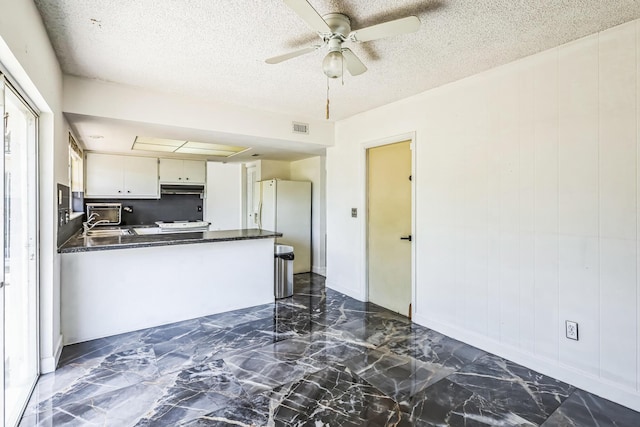 kitchen featuring dark countertops, under cabinet range hood, ceiling fan, a textured ceiling, and dark marble finish floors