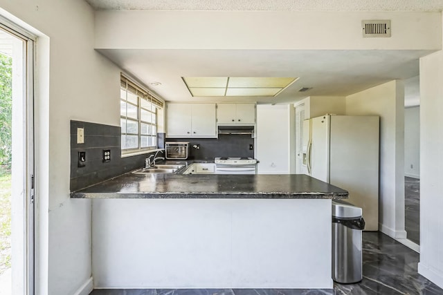 kitchen featuring white appliances, a sink, under cabinet range hood, dark countertops, and a peninsula