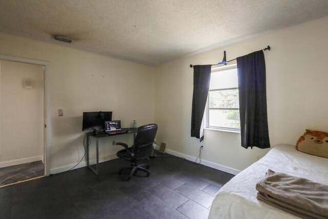 bedroom with a textured ceiling, baseboards, and a desk