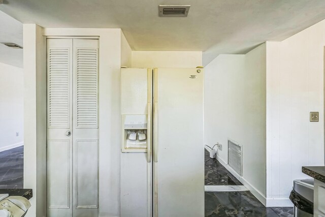 kitchen featuring white fridge with ice dispenser, baseboards, and dark marble finish flooring