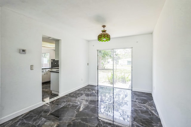 unfurnished dining area with plenty of natural light, baseboards, and dark marble finish flooring