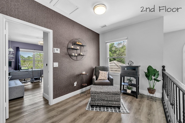 sitting room with an accent wall, a desk, wood finished floors, and baseboards