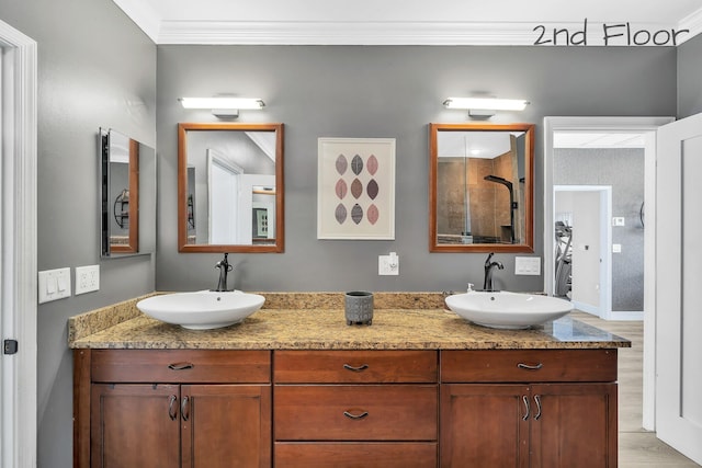 bathroom featuring ornamental molding, wood finished floors, double vanity, tiled shower, and baseboards