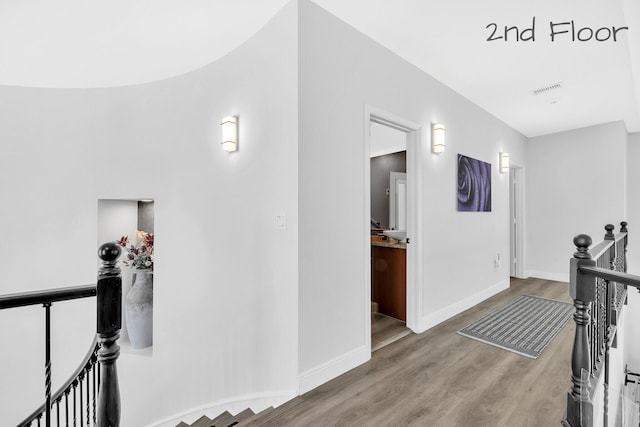 corridor featuring an upstairs landing, wood finished floors, and baseboards