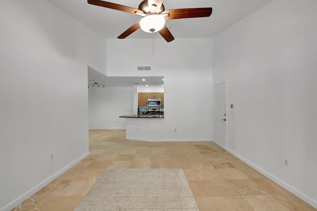 unfurnished living room with a towering ceiling, a ceiling fan, and baseboards