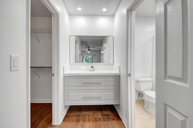 bathroom featuring toilet, vanity, wood finished floors, a spacious closet, and a textured ceiling