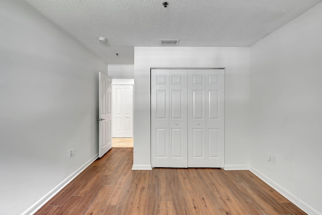 unfurnished bedroom featuring wood finished floors, baseboards, a closet, and a textured ceiling
