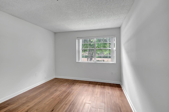 spare room with wood finished floors, a textured ceiling, and baseboards