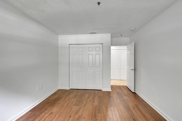 unfurnished bedroom with baseboards, wood finished floors, a closet, and a textured ceiling