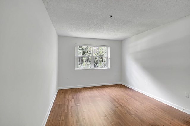 empty room featuring hardwood / wood-style flooring, a textured ceiling, and baseboards