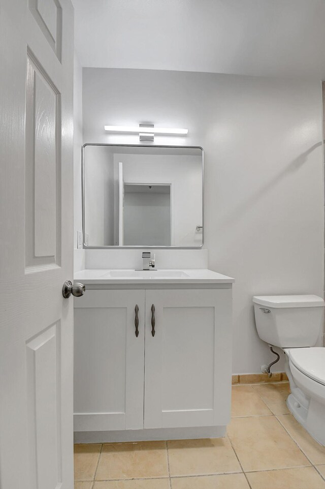 half bathroom featuring tile patterned flooring, toilet, vanity, and baseboards