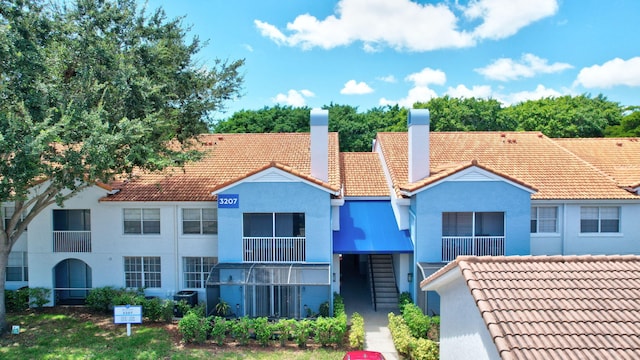 view of front facade featuring a tiled roof, a chimney, stucco siding, and central air condition unit