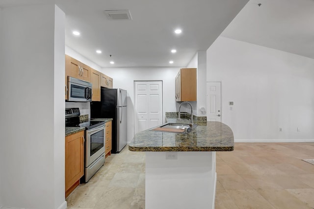 kitchen with appliances with stainless steel finishes, a sink, a peninsula, recessed lighting, and dark stone counters