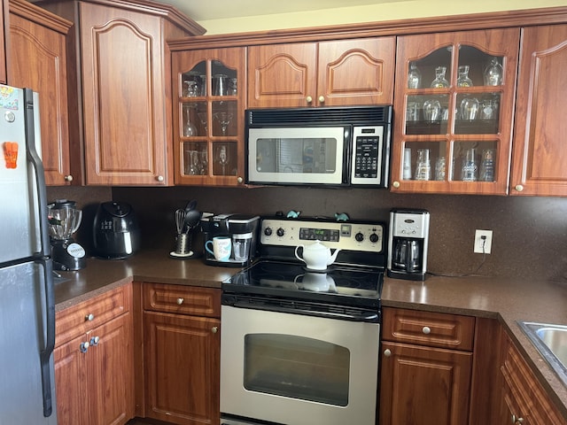 2950 Sunrise Lakes Dr W Unit 101, Sunrise, FL 33322 - kitchen featuring appliances with stainless steel finishes, glass insert cabinets, brown cabinets, and dark countertops
