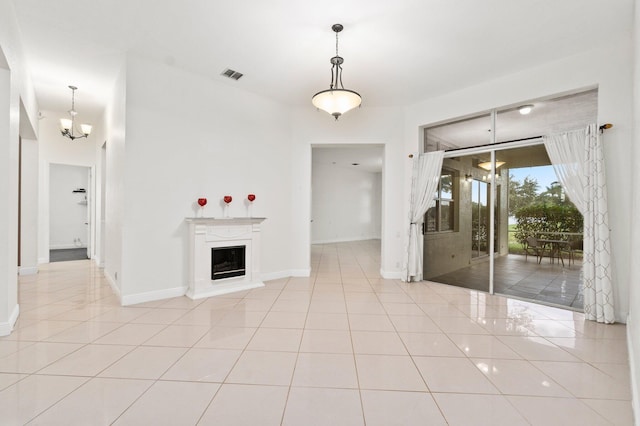 unfurnished living room featuring a chandelier, light tile patterned floors, a fireplace with raised hearth, and baseboards