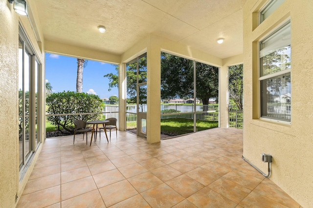 sunroom / solarium featuring tile patterned floors, healthy amount of natural light, a water view, and a textured ceiling