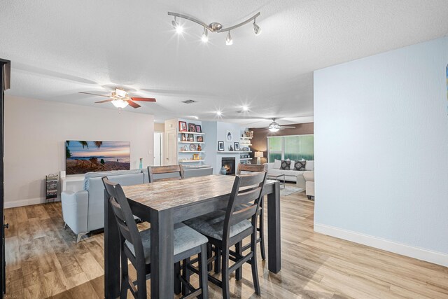 7503 NW 42nd St, Coral Springs, FL 33065 - dining area featuring ceiling fan, a lit fireplace, baseboards, light wood-style flooring, and a textured ceiling