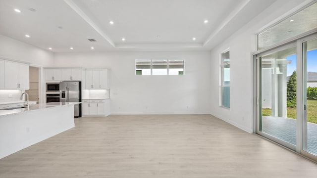 9143 SW Esule Way, Port Saint Lucie, FL 34987 - unfurnished living room featuring a sink, plenty of natural light, light wood-type flooring, recessed lighting, and a raised ceiling