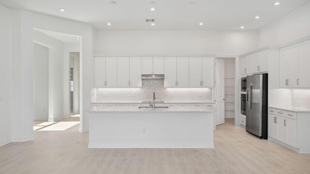 9143 SW Esule Way, Port Saint Lucie, FL 34987 - kitchen featuring appliances with stainless steel finishes, under cabinet range hood, decorative backsplash, a kitchen island with sink, and white cabinets