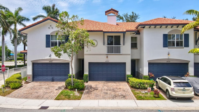 view of front of home with an attached garage, a tiled roof, stucco siding, a chimney, and driveway