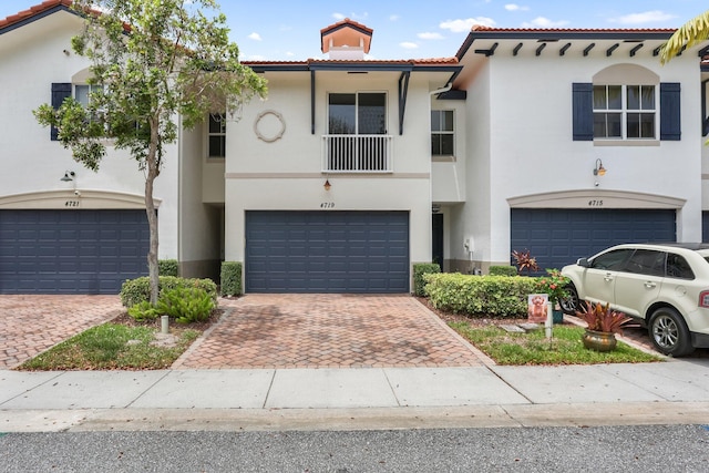 view of front of home with a garage, a tile roof, stucco siding, and decorative driveway