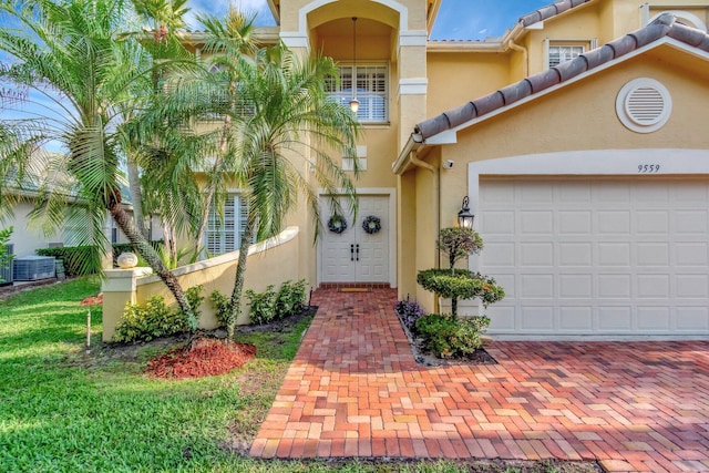 entrance to property featuring stucco siding, cooling unit, an attached garage, a tiled roof, and driveway