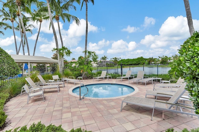 view of swimming pool featuring fence, a water view, a patio, and a jacuzzi