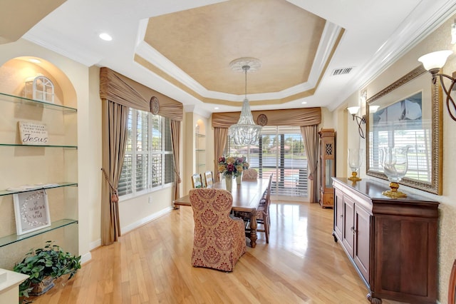dining room with a tray ceiling, a chandelier, crown molding, healthy amount of natural light, and light wood-style floors