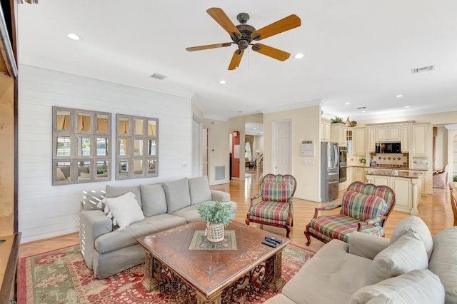 living area with ornamental molding, a ceiling fan, recessed lighting, light wood-style flooring, and baseboards