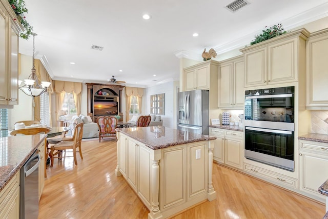 kitchen with cream cabinets, appliances with stainless steel finishes, open floor plan, ornamental molding, and a chandelier