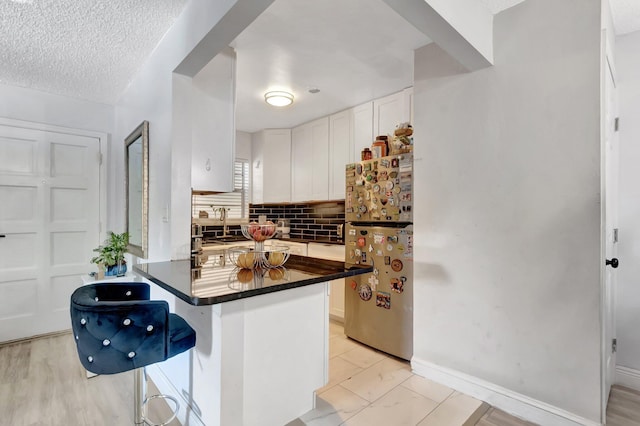 1124 NW 13th St Unit 208, Boca Raton, FL 33486 - kitchen featuring freestanding refrigerator, a breakfast bar, dark countertops, a peninsula, and backsplash