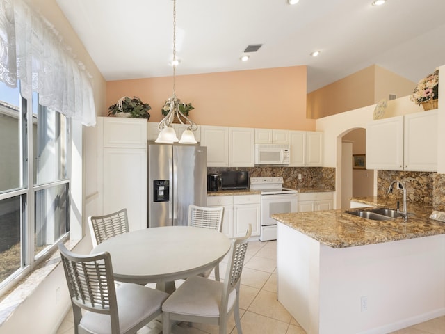 kitchen with white appliances, a sink, tasteful backsplash, arched walkways, and high vaulted ceiling