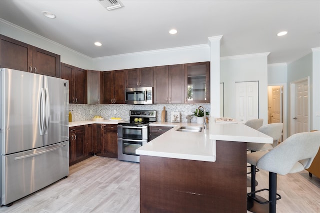 kitchen featuring appliances with stainless steel finishes, a sink, a kitchen breakfast bar, a peninsula, and crown molding