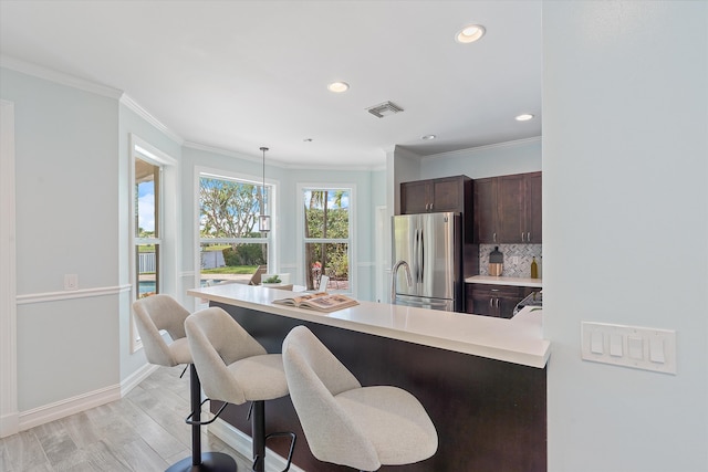 kitchen featuring freestanding refrigerator, light countertops, dark brown cabinetry, a kitchen breakfast bar, and decorative backsplash